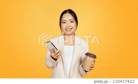 Glad millennial chinese lady in suit with cup of takeaway coffee, chatting on smartphone Glad millennial chinese lady in suit with cup of takeaway coffee, chatting on smartphone 110417422