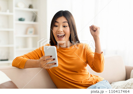 Overjoyed happy millennial asian woman celebrating success with smartphone 110417464