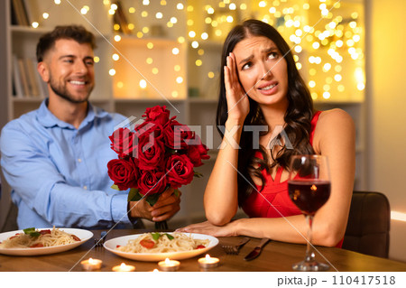 Man with roses smiling, woman stressed at dinner date Man with roses smiling, woman stressed at dinner date 110417518