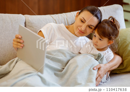 Mother and daughter with digital tablet relaxing on cozy couch Mother and daughter with digital tablet relaxing on cozy couch 110417638