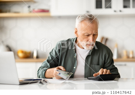 Concentrated senior male with cash in hand calculating finances at home 110417642