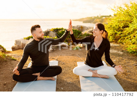Couple high-fiving during seaside yoga session at dawn Couple high-fiving during seaside yoga session at dawn 110417792