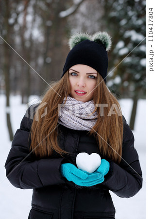 A teenage girl holds a heart made of snow in his hand 110417804