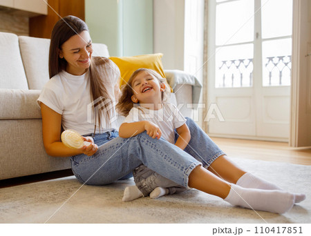 Cute little girl laughing while mother combing her hair at home 110417851
