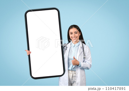 Positive female doctor with thumbs up holding huge mobile screen Positive female doctor with thumbs up holding huge mobile screen 110417891