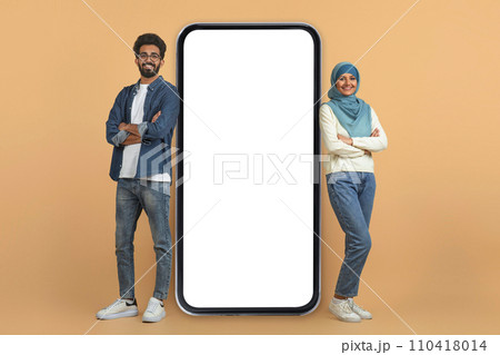 Mobile offer. Smiling muslim couple leaning on giant blank smartphone 110418014