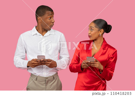 Surprised black couple with smartphones, both in holidays attire looking at each other Surprised black couple with smartphones, both in holidays attire looking at each other 110418203