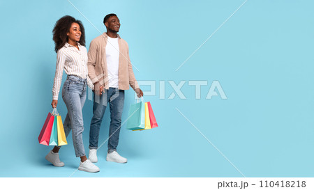 Joyful black couple with shopping bags on blue background, panorama Joyful black couple with shopping bags on blue background, panorama 110418218