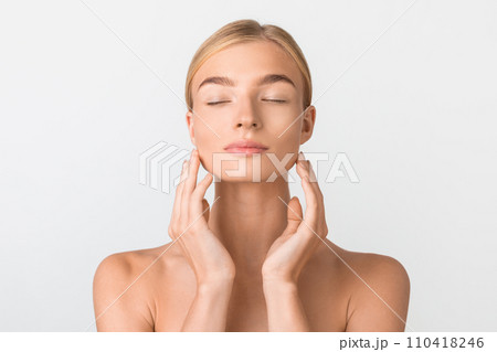 Beautiful young blonde lady touching smooth face skin, white backdrop 110418246