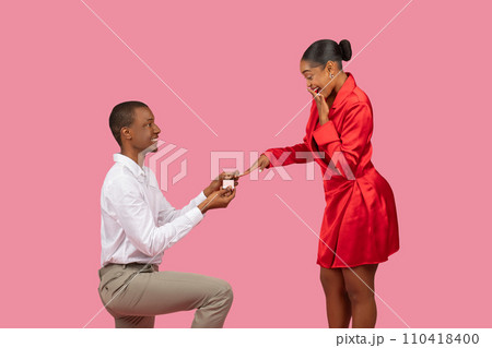Joyful marriage proposal, black man kneeling, woman in red dress excited Joyful marriage proposal, black man kneeling, woman in red dress excited 110418400