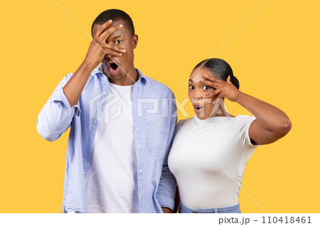 Shocked black couple with hands over eyes, humorous, yellow background 110418461