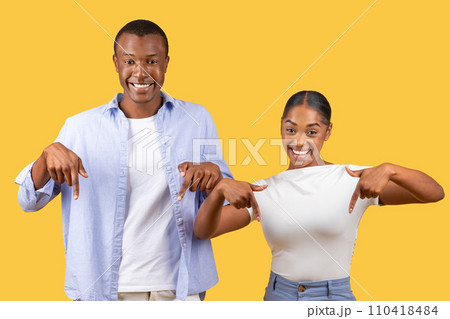 Joyful black couple pointing down, prideful smiles, yellow background Joyful black couple pointing down, prideful smiles, yellow background 110418484