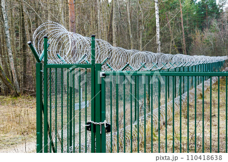A new green metal mesh fence with coiled barbed wire and gate around the restricted area 110418638