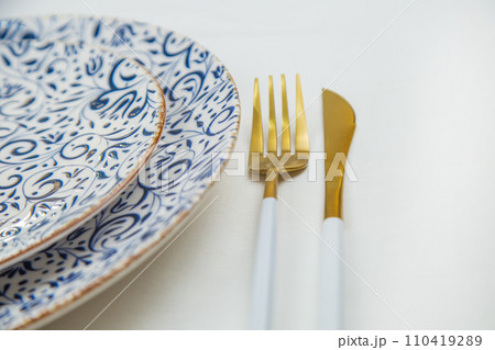 On the side, two serving plates with blue patterns on a white background stand one on one, part of the plates is visible, gold-white appliances are located on the side, a close-up side view on a white 110419289