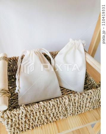 Wicker basket with white cotton bags on a wooden shelf against a white wall. Wicker basket with white cotton bags on a wooden shelf against a white wall. 110419331