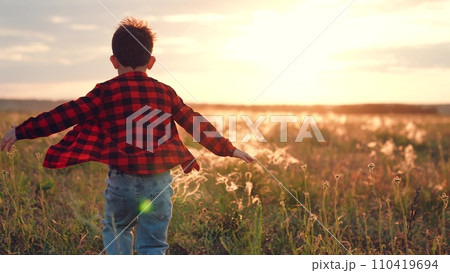 Positive boy runs along field with growing plants at sunset in autumn evening Positive boy runs along field with growing plants at sunset in autumn evening 110419694