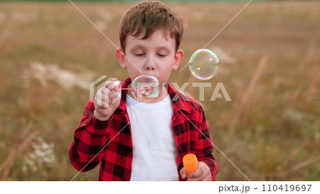 Happy boy finds happiness in blowing bubbles in field of cultivated plants Happy boy finds happiness in blowing bubbles in field of cultivated plants 110419697