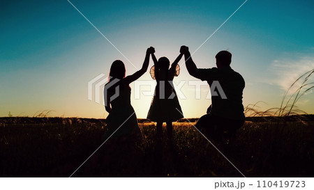 Family holds hands of daughter as squatting on park lawn enchanted by rays of sun 110419723