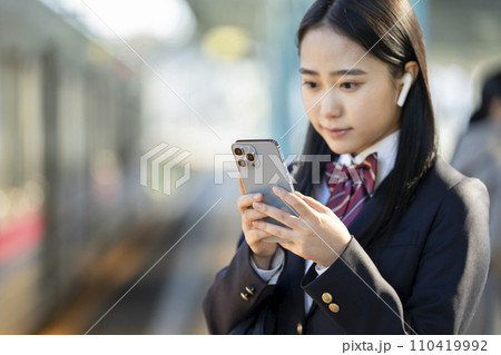 スマートホンの画面を見るイヤホンをつけた女子高校生　手元フォーカス 110419992