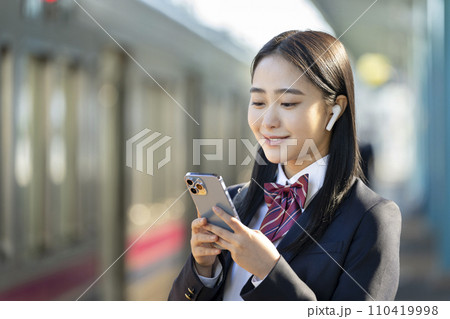 スマートホンの画面を見るイヤホンをつけた女子高校生　電車通学　イメージ 110419998