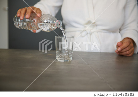 Close-up female hands pouring mineral water from a bottle into a drinking glass. Body and health care concept Close-up female hands pouring mineral water from a bottle into a drinking glass. Body and health care concept 110420282