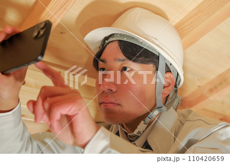 屋根裏で作業をする作業服姿の男性 110420659