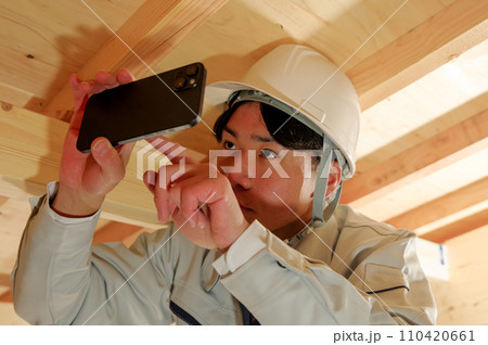 屋根裏で作業をする作業服姿の男性 110420661