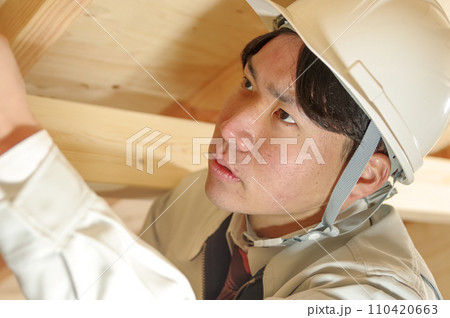 屋根裏で作業をする作業服姿の男性 110420663