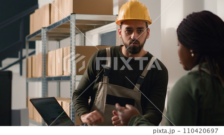 Storage facility warehouse supervisor carrying out the logistics of receiving, processing, storing and sending inventory according to purchase orders and shipping schedules, helped by diligent trainee 110420697