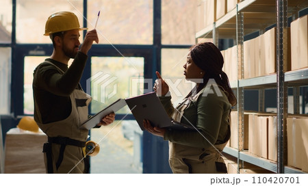 Head of logistics and worker perform warehouse inventory controls, keeping quality standards high. Skillful experts in storage facility preparing to ship parcels, crosschecking delivery info 110420701