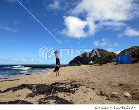Handstanding at Makapuu Beach with tents and lighthouse on cliff in the distance Handstanding at Makapuu Beach with tents and lighthouse on cliff in the distance 110422537