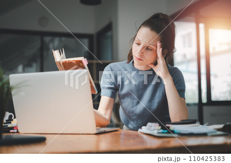 Businesswoman is serious at work causing headaches and stressed out with documents with a laptop at the office Businesswoman is serious at work causing headaches and stressed out with documents with a laptop at the office 110425383