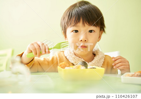 美味しそうにお弁当を食べる幼い男の子 美味しそうにお弁当を食べる幼い男の子 110426107