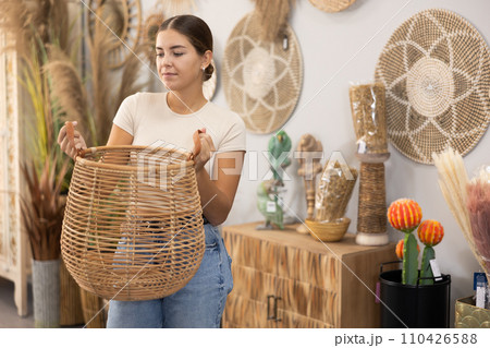 Girl looks at wicker basket in furniture store. 110426588
