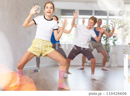 Cheerful friendly school children spreading hands wild apart while practicing active dance with their middle-aged parents in dance hall 110426606