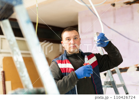 Electrician with pliers in hand prepares electrical wiring in house under construction Electrician with pliers in hand prepares electrical wiring in house under construction 110426724