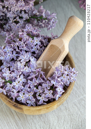 Wooden Bowl with wooden spoon of fresh purple lilac petals with branch of blooming lilac. Lilac flowers fragrance. Concept for spa wellness and aromatherapy. Copy space Still life composition 110428217