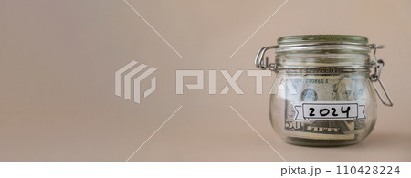 Glass jar full of American currency dollars cash banknote with text 2024 year. Preparation saving money. Moderate consumption and economy 110428224