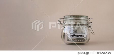 Glass jar full of American currency dollars cash banknote with text RETIREMENT. Preparation saving money. Moderate consumption and economy Glass jar full of American currency dollars cash banknote with text RETIREMENT. Preparation saving money. Moderate consumption and economy 110428239