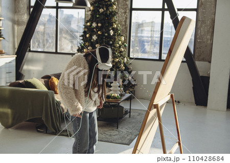 In a Christmas setting, a young woman in light clothing and a virtual reality headset stands in front of the mirror. 110428684