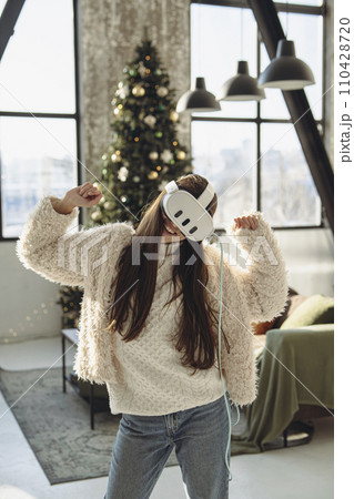 In front of a Christmas tree, a lovely young lady wears a virtual reality headset. In front of a Christmas tree, a lovely young lady wears a virtual reality headset. 110428720