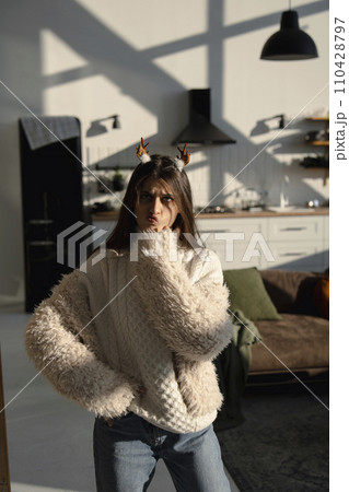 In a sunlit apartment, a vibrant young lady dons a Christmas reindeer mask. In a sunlit apartment, a vibrant young lady dons a Christmas reindeer mask. 110428797