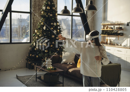 Engrossed in an online game, a lovely young lady wears a virtual reality headset in her apartment. 110428805