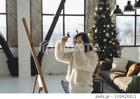 A joyful expression graces the face of a lively young woman in a Christmas reindeer mask at home. A joyful expression graces the face of a lively young woman in a Christmas reindeer mask at home. 110428811