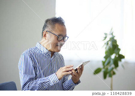 リビングにてタブレット端末を使用する日本人のシニア男性 110428839