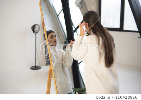 Engaged in a holiday atmosphere, a beautiful young lady does makeup by the mirror. 110428916
