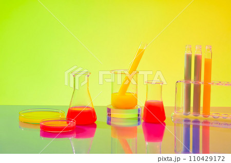 Colorful liquids are contained in test tubes, petri dishes, beakers and Erlenmeyer flasks on a green-yellow gradient background. Inside the laboratory. 110429172