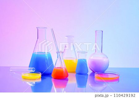 Front view of colorful liquids inside an erlenmeyer flask, petri dish and high-necked spherical flask on a purple-blue gradient background. Inside the laboratory. Front view of colorful liquids inside an erlenmeyer flask, petri dish and high-necked spherical flask on a purple-blue gradient background. Inside the laboratory. 110429192