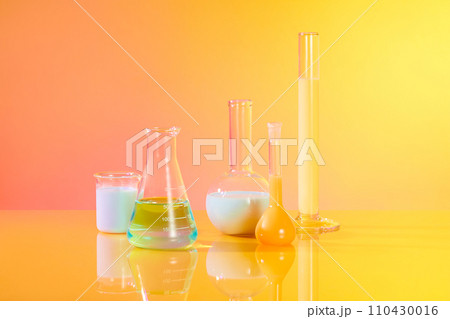 Front view of different types of laboratory glassware filled with colorful liquid decorated over gradient yellow and pink background. Laboratory experience and research concept  110430016