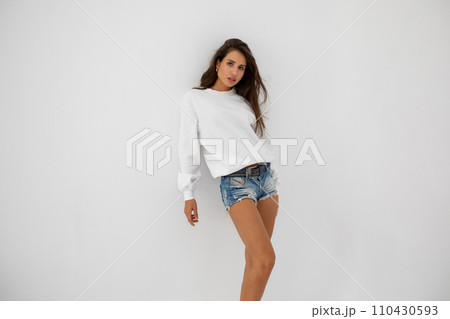 Beautiful girl in shorts and a white sweatshirt posing on a white background 110430593